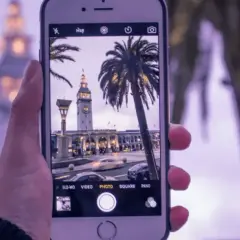 Zdjęcia iPhone uchwyciły wieżę zegarową i palmy w miejskim krajobrazie.