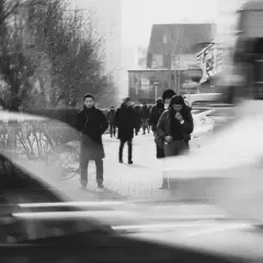Ludzie na chodniku, rozmyte samochody i drzewa. Długi czas naświetlania (shutter speed) uchwycił ruch uliczny i miejską atmosferę.