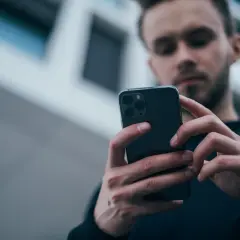 Mężczyzna z uwagą przegląda smartfon, zastanawiając się, jaki wybrać telefon.