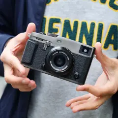 Dłonie trzymają aparat Fujifilm xpro3 z obiektywem.