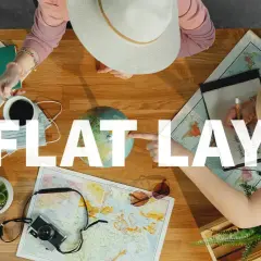 Widok z góry na stół z mapami, globusem, aparatem, notatnikiem i kawą. Dwie osoby planują podróż, tworząc idealny **flat lay**.