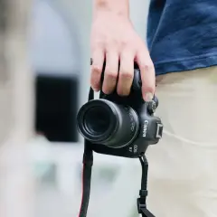Dłoń trzyma aparat Canon EOS R7 z obiektywem, idealny do fotografii krajobrazowej i portretowej dzięki matrycy APS-C.