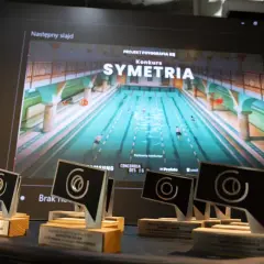 Nagrody konkursu "Symetria" na tle ekranu z basenem. To inspiracja dla uczestników kursu fotografii online.