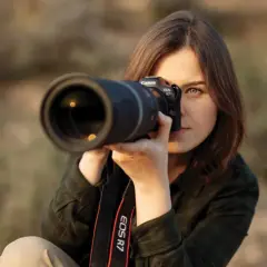 Kobieta z aparatem Canon EOS R7, skupiona na kadrze. Dopasowuje ustawienia aparatu, by uchwycić idealny moment.