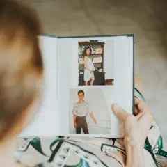 Starsza osoba przegląda album ze zdjęciami. Na górze zdjęcie młodej kobiety w ciąży, na dole młody mężczyzna w koszuli.
