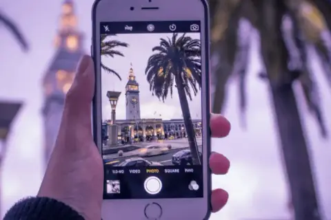 Zdjęcia iPhone uchwyciły wieżę zegarową i palmy w miejskim krajobrazie.