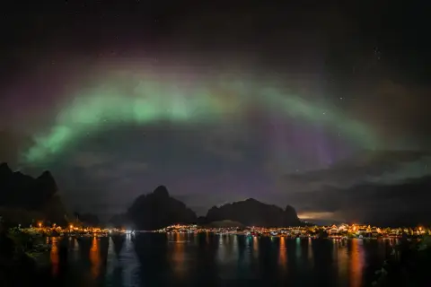 Zorza polarna nad fiordem, z miasteczkiem w oddali. Chcesz wiedzieć, jak zrobić zdjęcie zorzy polarnej telefonem?