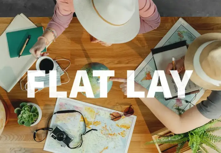 Widok z góry na stół z mapami, globusem, aparatem, notatnikiem i kawą. Dwie osoby planują podróż, tworząc idealny **flat lay**.