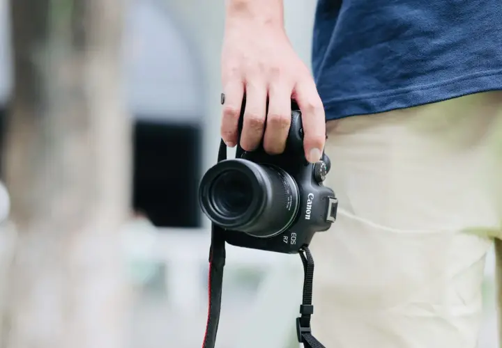 Dłoń trzyma aparat Canon EOS R7 z obiektywem, idealny do fotografii krajobrazowej i portretowej dzięki matrycy APS-C.