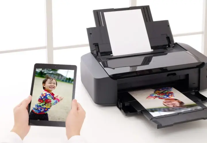 Uchwyć radość dziecka, drukując zdjęcia w domu. Tablet pokazuje uśmiechniętą twarz, a drukarka właśnie wydrukowała podobny kadr.