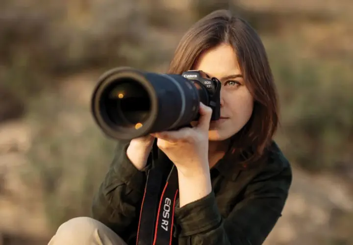 Kobieta z aparatem Canon EOS R7, skupiona na kadrze. Dopasowuje ustawienia aparatu, by uchwycić idealny moment.
