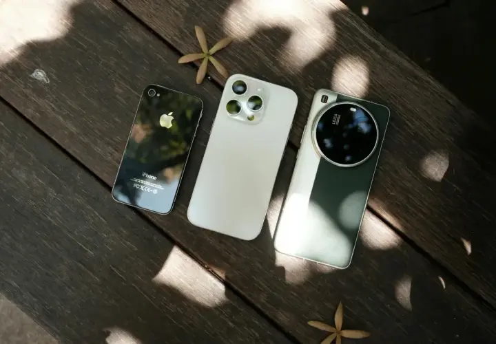 Trzy smartfony fotograficzne: stary iPhone, biały iPhone i zielony Huawei z aparatem Leica, leżą na drewnianym stole.