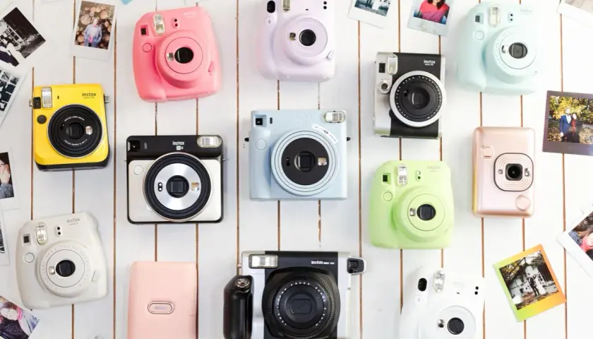 Różne rodzaje aparatów Instax w jaskrawych kolorach: żółty, różowy, fioletowy, niebieski, zielony, biały, srebrny i pudrowy róż.