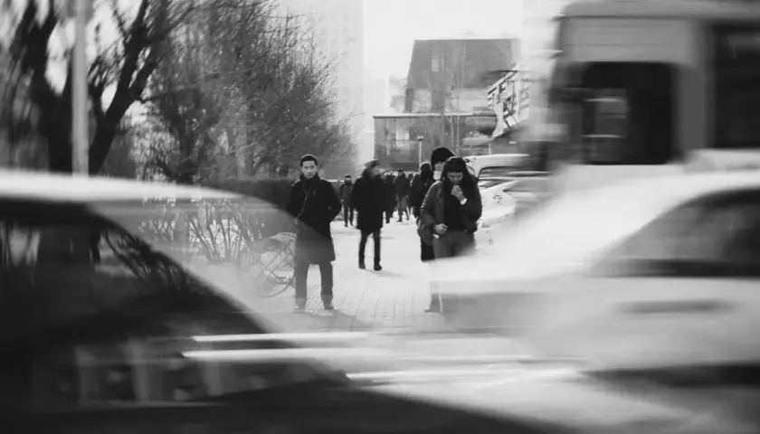 Ludzie na chodniku, rozmyte samochody i drzewa. Długi czas naświetlania (shutter speed) uchwycił ruch uliczny i miejską atmosferę.