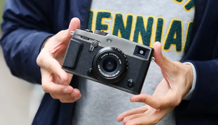 Dłonie trzymają aparat Fujifilm xpro3 z obiektywem.