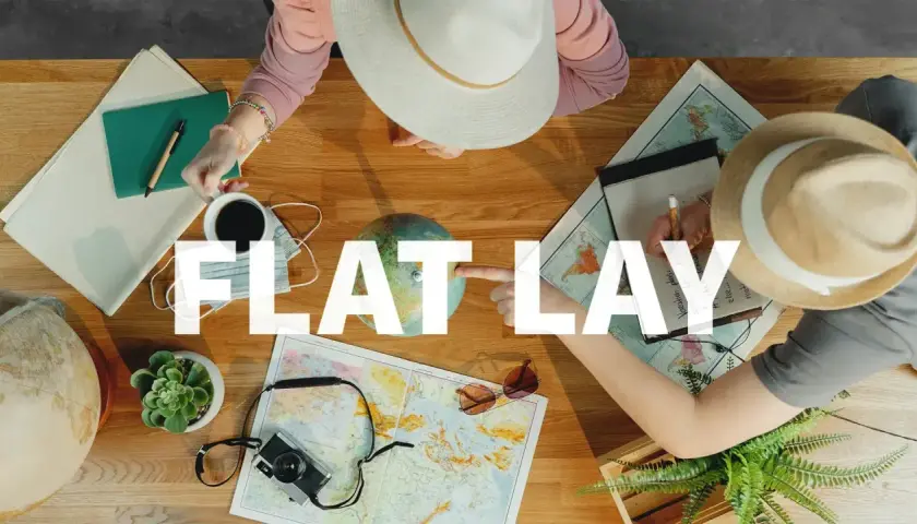 Widok z góry na stół z mapami, globusem, aparatem, notatnikiem i kawą. Dwie osoby planują podróż, tworząc idealny **flat lay**.