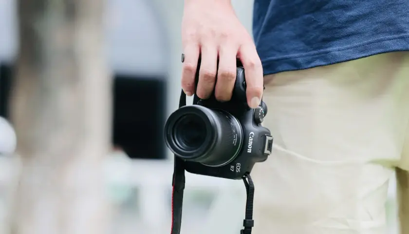 Dłoń trzyma aparat Canon EOS R7 z obiektywem, idealny do fotografii krajobrazowej i portretowej dzięki matrycy APS-C.