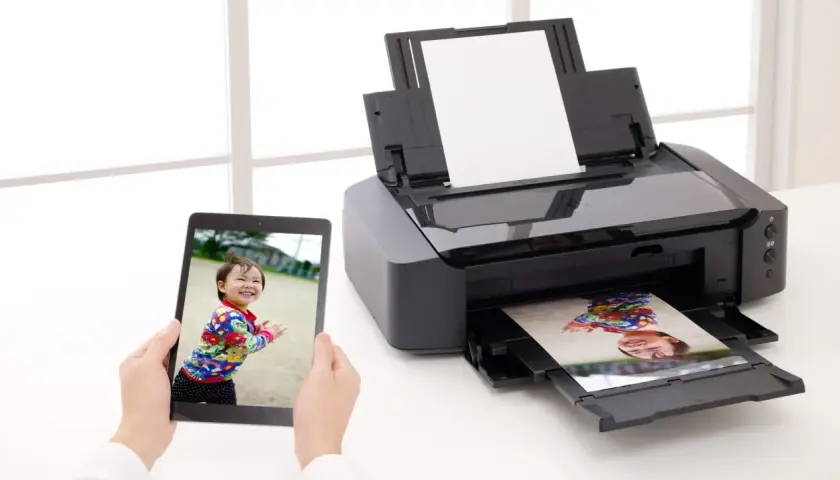 Uchwyć radość dziecka, drukując zdjęcia w domu. Tablet pokazuje uśmiechniętą twarz, a drukarka właśnie wydrukowała podobny kadr.