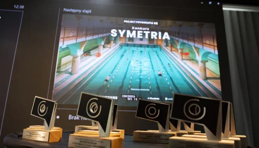 Nagrody konkursu "Symetria" na tle ekranu z basenem. To inspiracja dla uczestników kursu fotografii online.