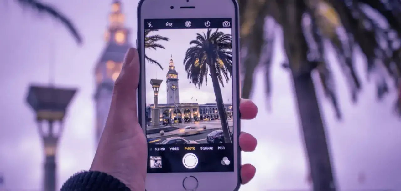 Zdjęcia iPhone uchwyciły wieżę zegarową i palmy w miejskim krajobrazie.