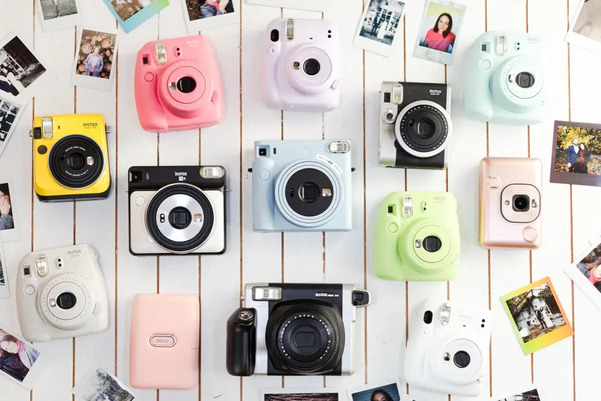 Różne rodzaje aparatów Instax w jaskrawych kolorach: żółty, różowy, fioletowy, niebieski, zielony, biały, srebrny i pudrowy róż.