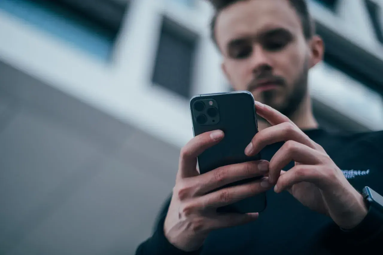 Mężczyzna z uwagą przegląda smartfon, zastanawiając się, jaki wybrać telefon.