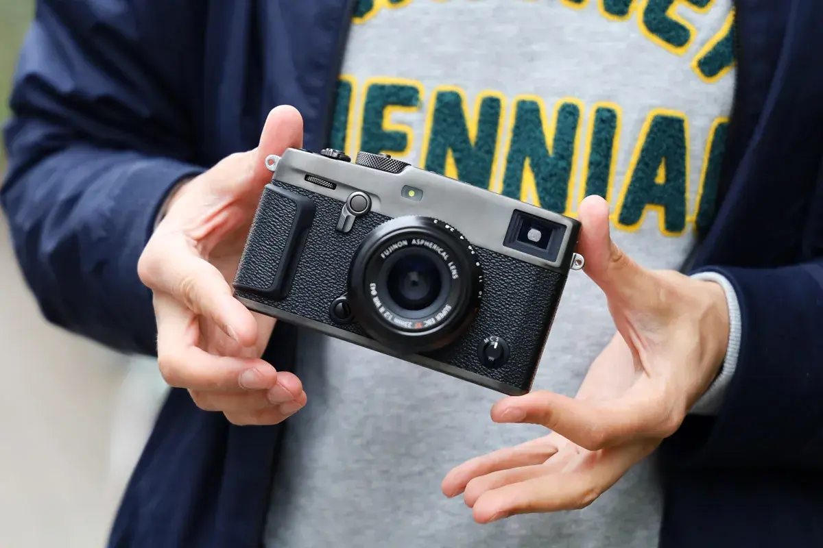 Dłonie trzymają aparat Fujifilm xpro3 z obiektywem.
