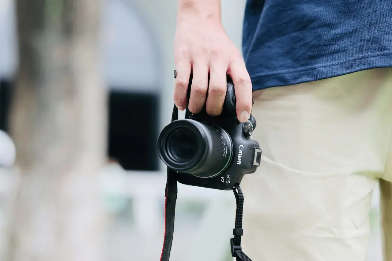 Dłoń trzyma aparat Canon EOS R7 z obiektywem, idealny do fotografii krajobrazowej i portretowej dzięki matrycy APS-C.