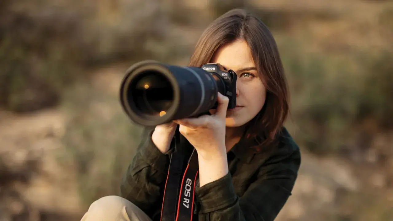 Kobieta z aparatem Canon EOS R7, skupiona na kadrze. Dopasowuje ustawienia aparatu, by uchwycić idealny moment.