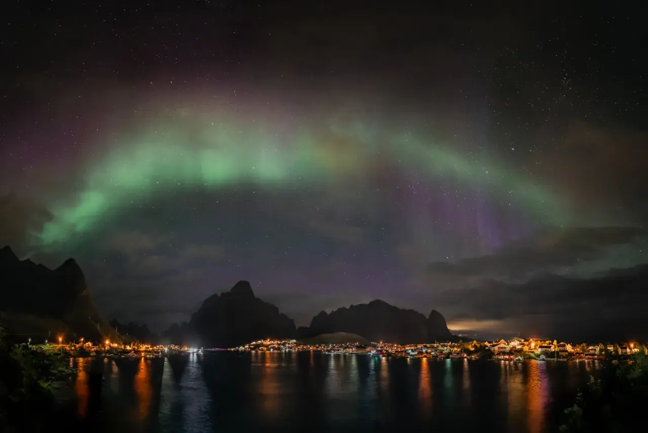Zorza polarna nad fiordem, z miasteczkiem w oddali. Chcesz wiedzieć, jak zrobić zdjęcie zorzy polarnej telefonem?