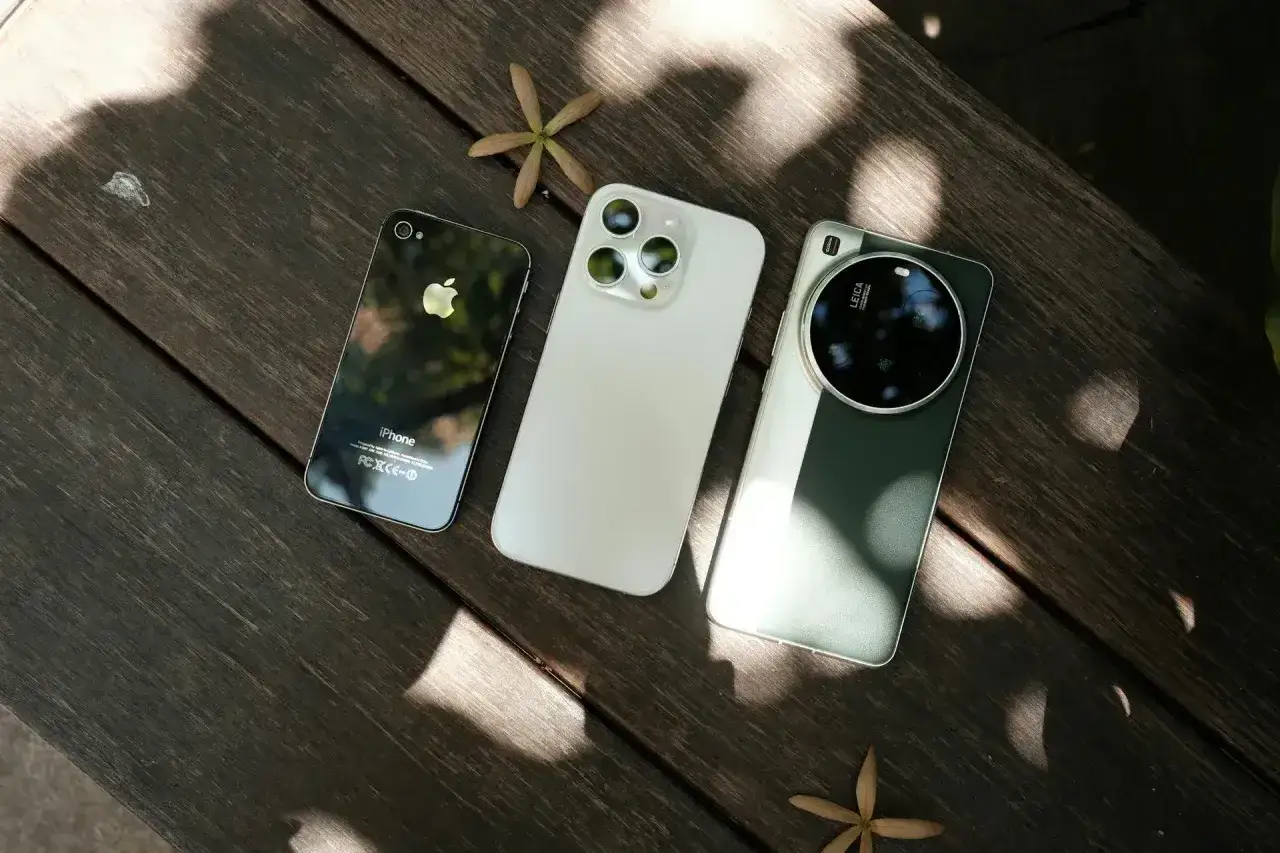 Trzy smartfony: stary iPhone, biały iPhone i zielony telefon z aparatem Leica. Porównanie ewolucji fotosmartfonów.