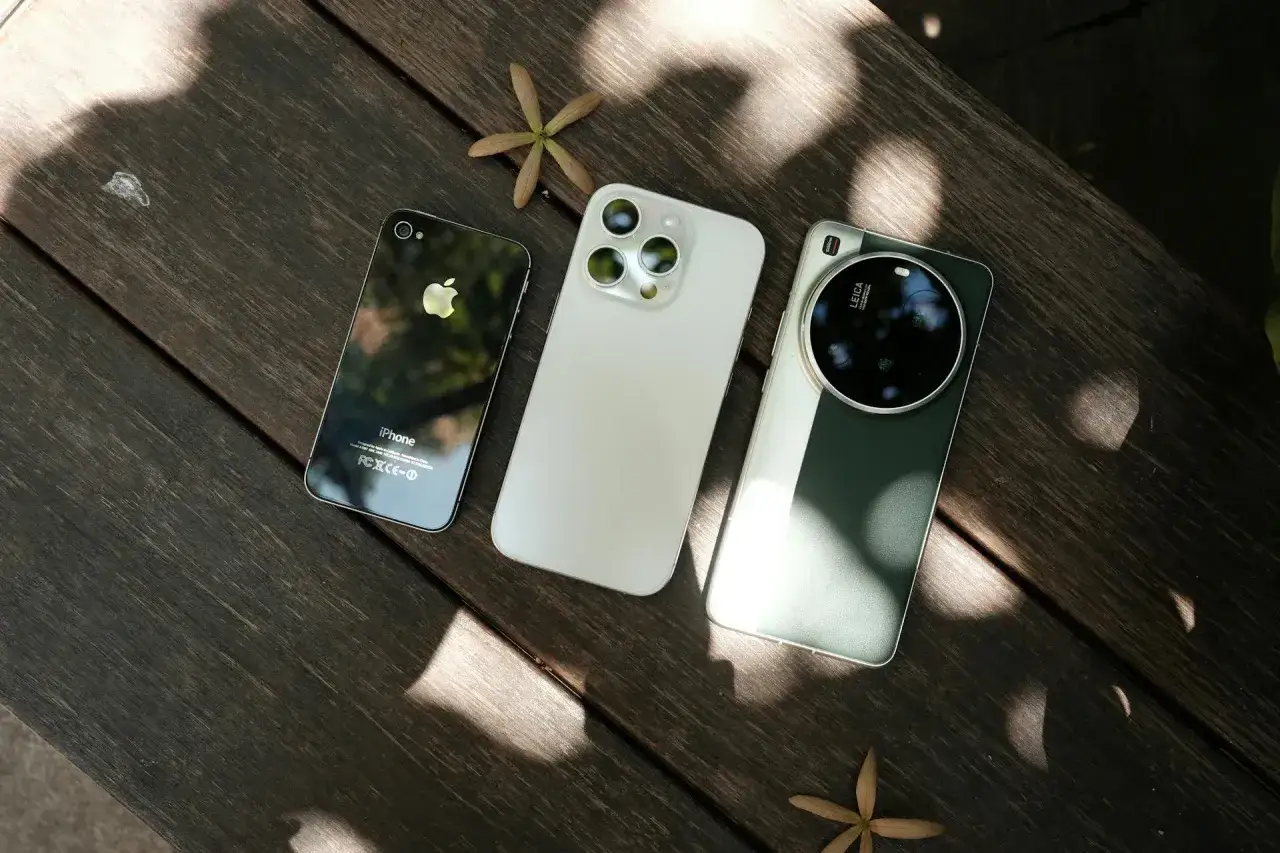Trzy telefony: stary iPhone, nowy iPhone i telefon z aparatem Leica. Zdjęcia iPhone'ów pokazują ewolucję technologii.
