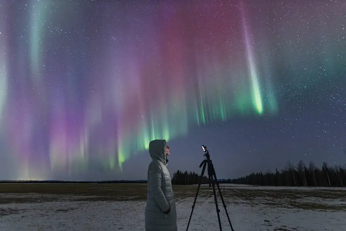 Osoba z telefonem na statywie podziwia zorzę polarną. To inspiracja, jak zrobić zdjęcie zorzy polarnej telefonem.